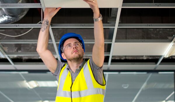 En byggnadsarbetare som installerar en takfläkt på ett kontor.