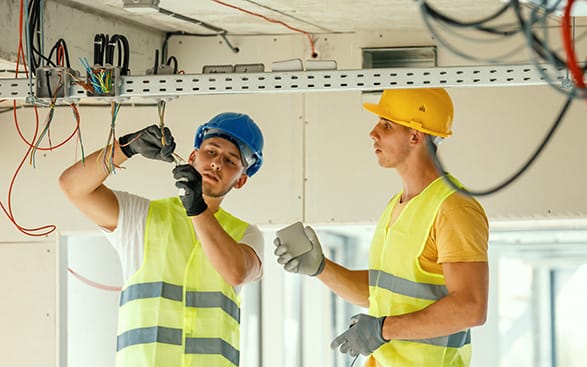 Två byggnadsarbetare som arbetar med elektriska ledningar i en byggnad.