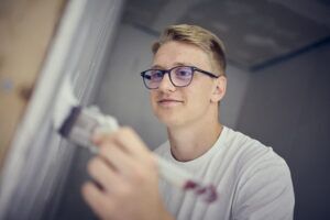 En ung man med glasögon målar en vägg.