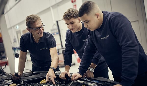Tre män som arbetar på en bilmotor i ett garage.