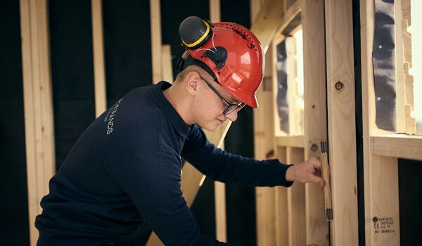 En man i en röd hatt arbetar på en vägg.