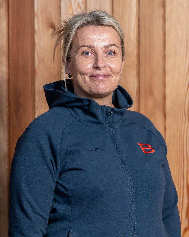 En kvinna i en blå hoodie som står framför en trävägg.