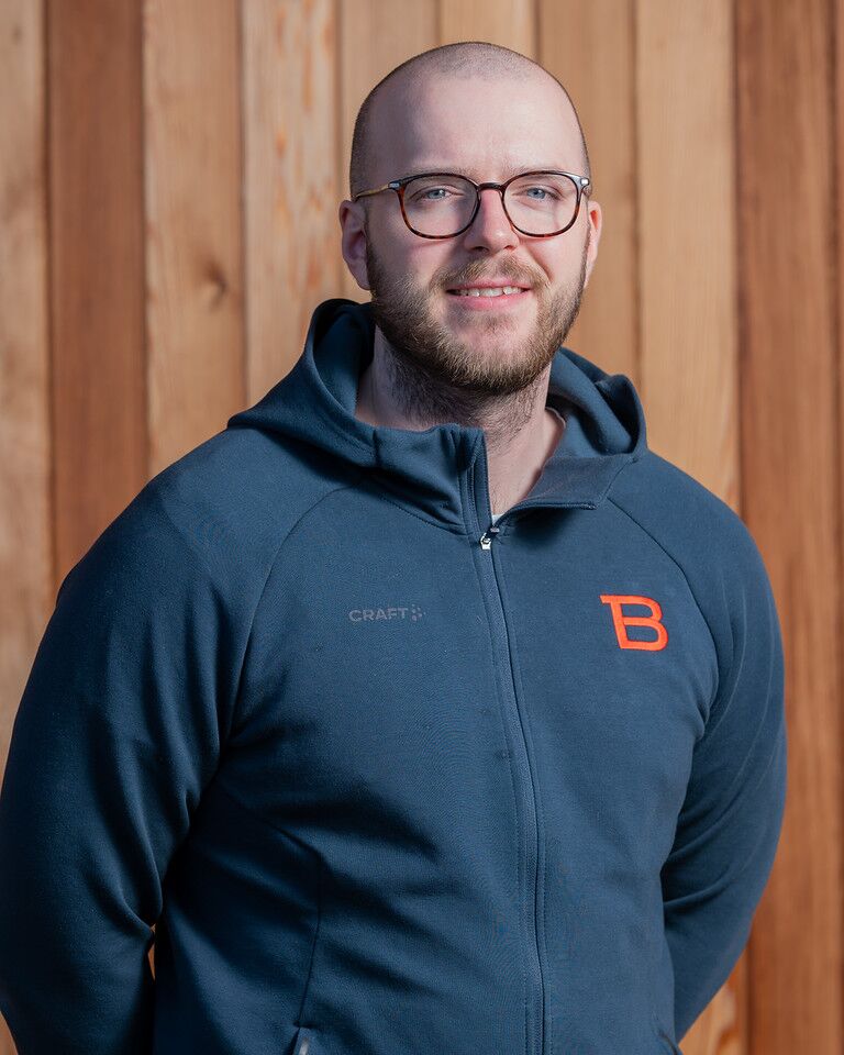 En man i en blå hoodie som står framför en trävägg.