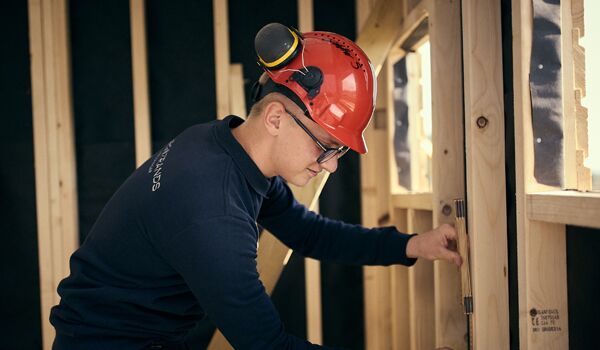 husbyggnad_600x350 En man i en röd hatt arbetar på en vägg.