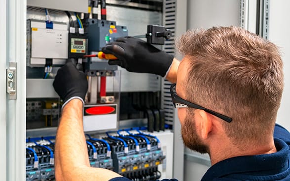 iStock-1165561132-587×367-opt En man arbetar på en elektrisk panel.