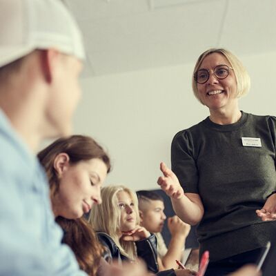 service-600×600 En kvinna pratar med en grupp människor i ett klassrum.
